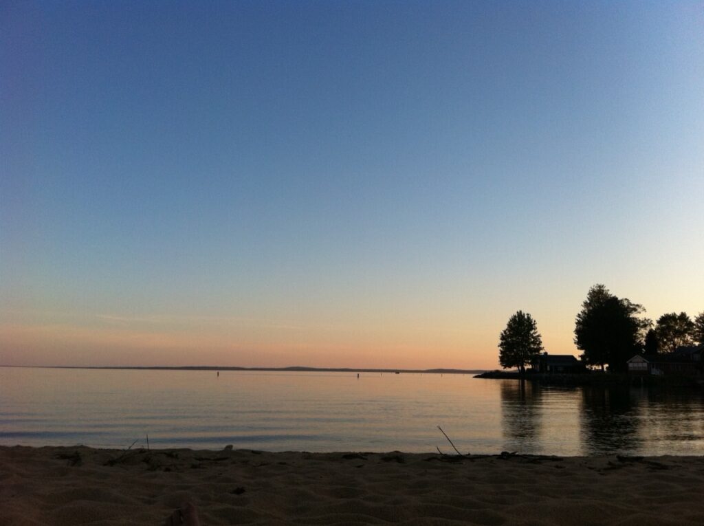 Calm evening water and sandy shoreline near the Songo River entrance to Sebago Lake.