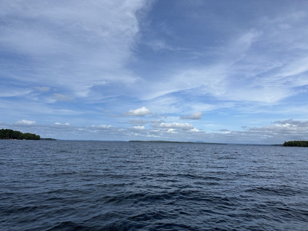 A broad view across Sebago Lake beneath a cloud-streaked sky, with a low wooded shoreline in the distance.