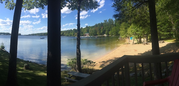 A lakeside view with a sandy beach, picnic tables, and a deck overlooking the water.