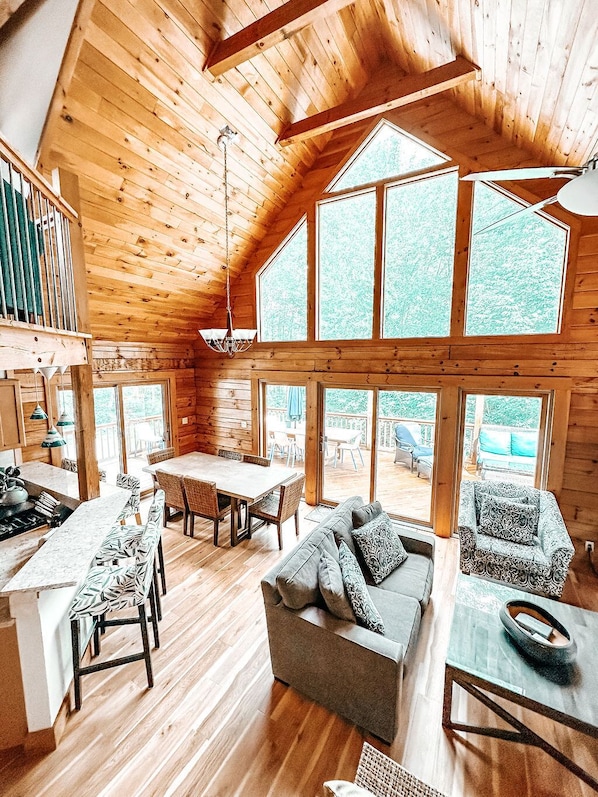 A spacious cabin with a high ceiling, large windows, a dining area, and a cozy seating area.