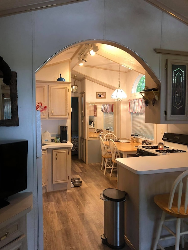 A compact kitchen with wooden cabinets, a central island with a stove, and a dining area with chairs.