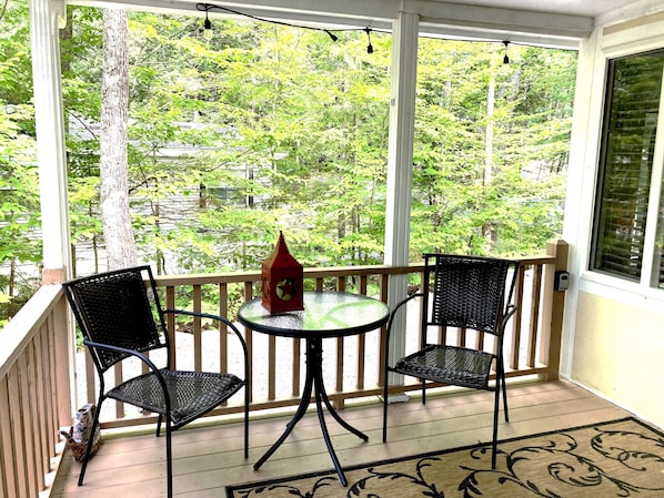 A covered porch with two black wicker chairs and a small table, overlooking a lush green landscape.