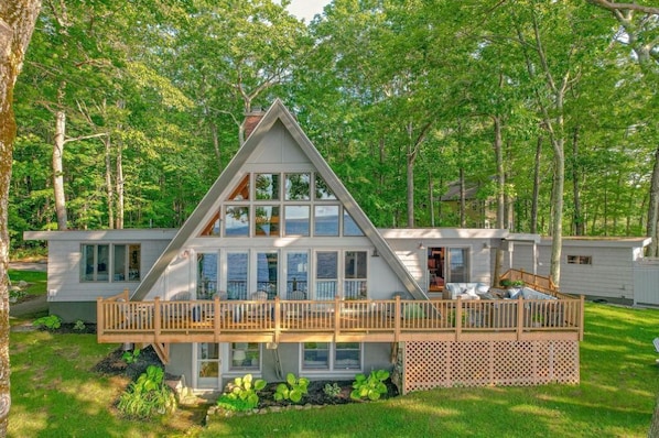 A modern, two-story house with a large deck and a view of the surrounding forest.