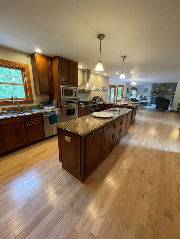 A spacious kitchen with wooden cabinets, a central island, and a stone fireplace in the background.