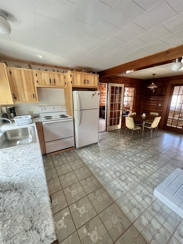 A kitchen with wooden cabinets, a white stove, a refrigerator, and a dining area with a table and chairs.