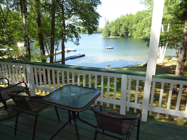 A covered deck with a table and chairs overlooking a lake.