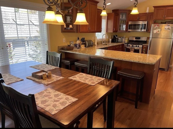 A kitchen with wooden cabinets, a granite countertop, stainless steel appliances, and a dining area with a wooden table and chairs.