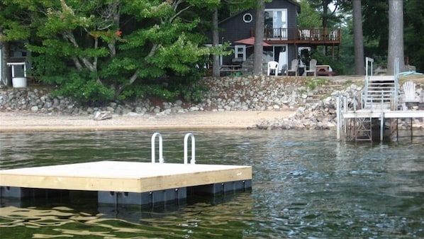 A wooden dock extending into a body of water with a house and trees in the background.