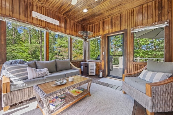 A wooden cabin with a covered porch, wicker furniture, and a view of the forest.