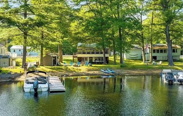 A lakeside property with a dock, boats, and a house surrounded by trees.