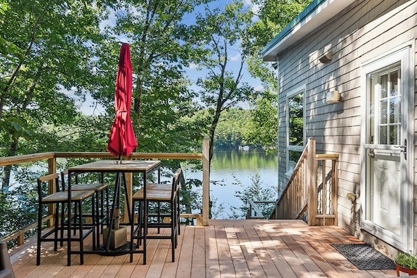 A wooden deck with a table and chairs, overlooking a lake.