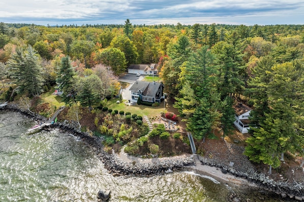 A house surrounded by dense forest with a rocky shoreline and a small dock.