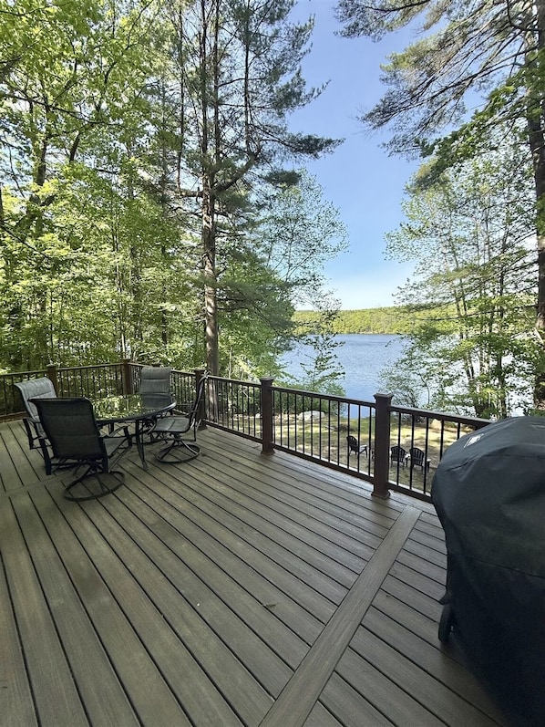 A wooden deck with outdoor furniture overlooking a lake, surrounded by trees.