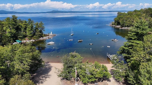 A coastal area with boats anchored near a lighthouse, surrounded by dense forest.