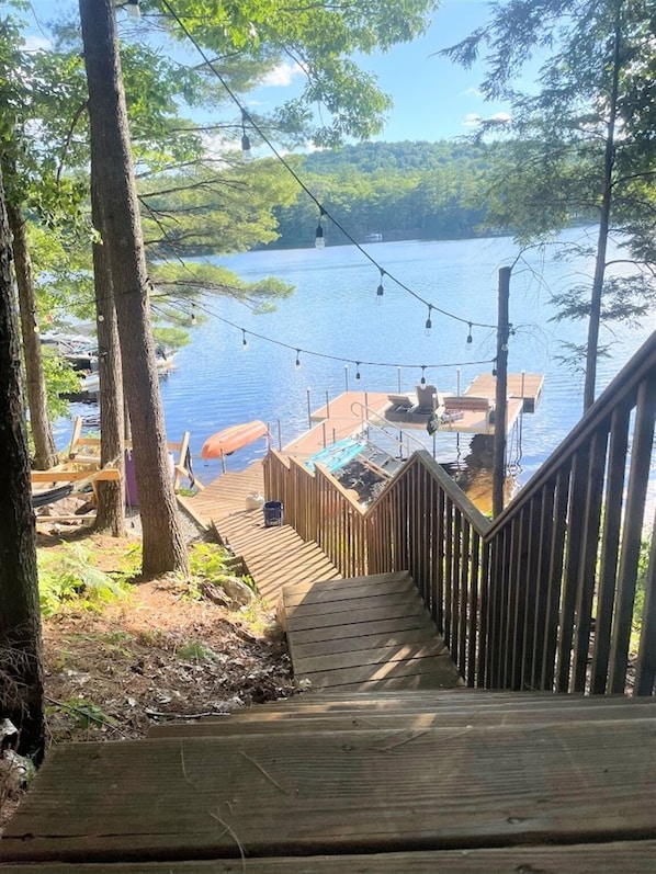 A wooden deck leading to a dock with chairs and a table, overlooking a lake.