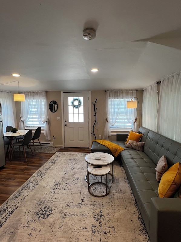 A living room with a sofa, a coffee table, a dining area with chairs, a chandelier, and a door with a wreath.